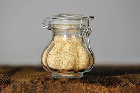 A small, decorative glass jar with garlic flakes, showcasing its fine texture and color on a rustic