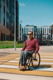 A man in a wheelchair navigates a crosswalk marked with yellow lines in a contemporary city