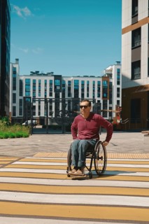 A person using a wheelchair navigates a brightly painted crosswalk in a modern urban area.
