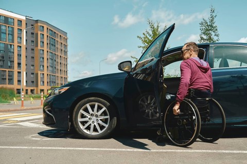 A man in a wheelchair is using his arms to propel himself into a parked vehicle with an open door.