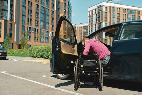 A man moves to a wheelchair from a car parked at a lot for people with disabilities in a