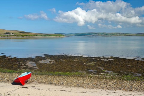 Red boat on the beach with a distant view of the calm sea and a cloudy summer landscape, Hoy,