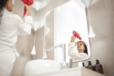 A woman wearing a bathrobe uses a hairdryer while looking in the mirror. The chic bathroom features