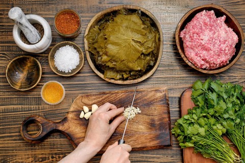 Preparing dolma at home involves chopping garlic and herbs while surrounded by fresh grape leaves