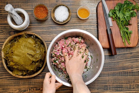 At home, a person mixes seasoned minced meat with rice and herbs in a large bowl. Surrounding the