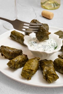 Dolma is being prepared in a cozy kitchen. Stuffed grape leaves are arranged on a plate,