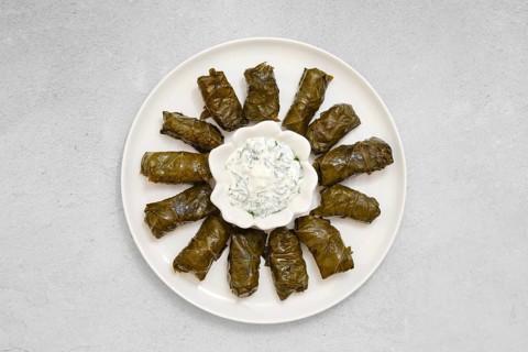 Freshly prepared dolma sits on a plate, featuring stuffed vine leaves neatly arranged. A bowl of