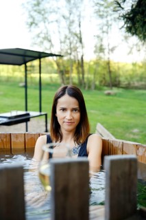 A woman enjoys a serene moment in a wooden hot tub, immersed in warm water, while surrounded by