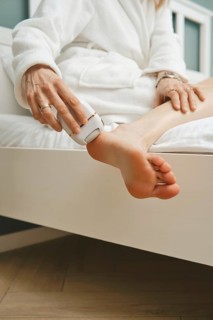 Close-up view of peeling dead skin off heel with handheld electric exfoliating machine in bedroom