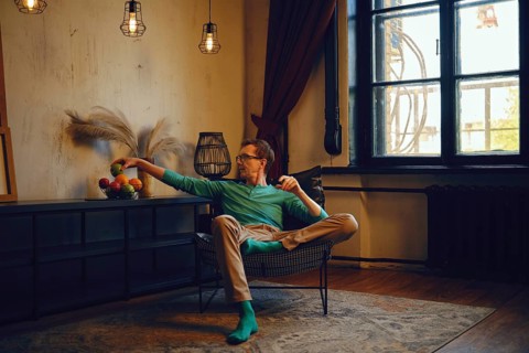 A man sits comfortably in a contemporary chair, casually extending his arm to grab fruit from a
