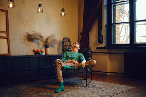 A man relaxes in a modern chair in a well-lit living space filled with warm tones. Sunlight streams