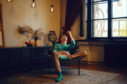 A man sits comfortably in a chair, gazing thoughtfully at an apple in his hand. Soft lighting and
