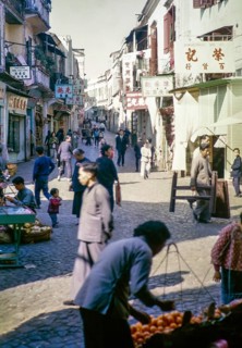 Busy shopping street Cantonese shop signs, with people walking traders with fruit stalls, Macau,