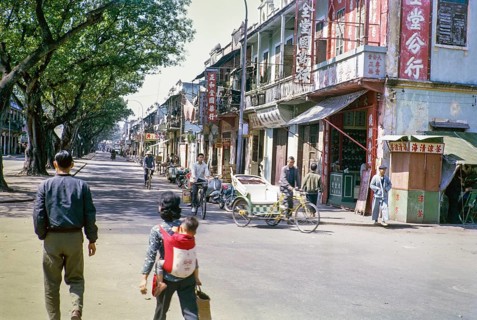 People walling and cycles in tree lined street with small shops, Macau, Asia 1964
