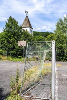 Old sports field, with asphalt floor, weeds reclaiming the field, apparently abandoned football