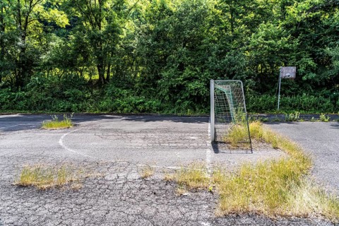 Old sports field, with asphalt floor, weeds reclaiming the field, apparently abandoned football