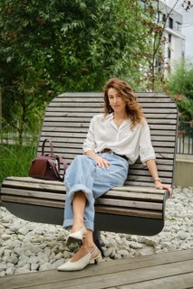 A woman sits comfortably on a unique wooden bench in a modern urban garden. She wears casual