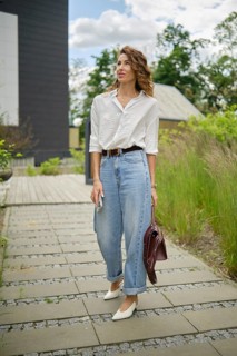 A young woman is walking along a stone path, wearing a white shirt and light blue baggy jeans. She