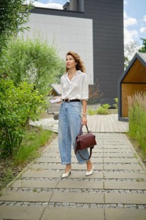 A woman wearing a white shirt and high-waisted jeans strolls through a landscaped path surrounded