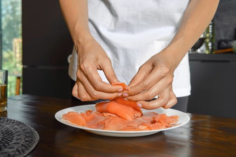 Hands expertly handle smoked salmon fillets on a plate, showcasing a focus on healthy food