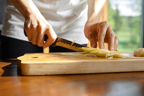 Unrecognizable person skillfully slices fresh ginger on a wooden cutting board in a well-lit