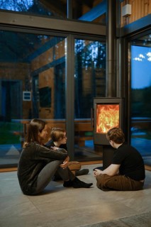 A family of three gathers around a glowing fireplace inside a contemporary cabin. The warm ambiance