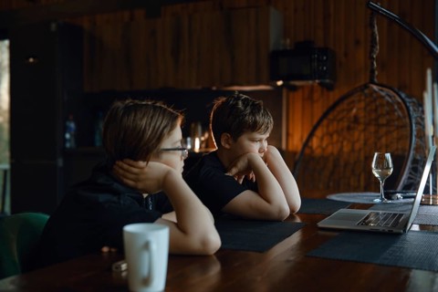 Two children are seated at a wooden table in a warm, rustic environment, deeply engaged with a