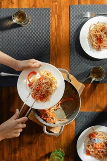 Close-up view of female hands serving pasta with stir fry spicy beef with vegetables on a plate