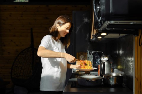 A woman takes out fried vegetables from the pan with kitchen tongs standing by the stove in a