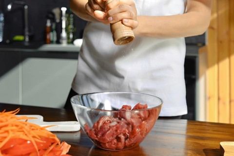 Unrecognizable person is adding freshly ground salt to a bowl of diced meat, preparing for a