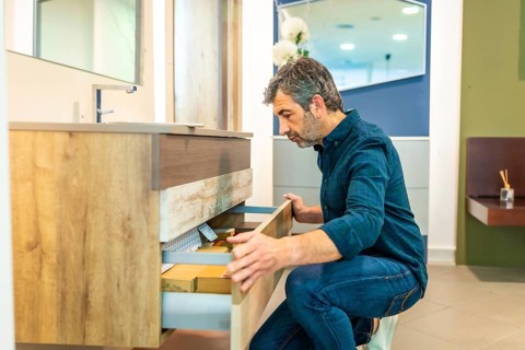 Mature man crouching, opening drawers of a bathroom vanity, checking quality and organization in a