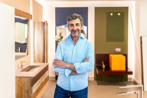 Confident salesman smiling with crossed arms while posing in a bathroom furniture store, showcasing