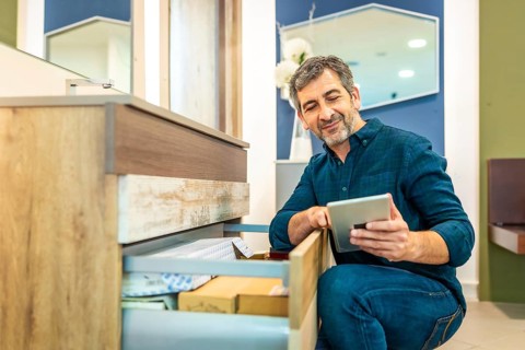 Smiling mature man using a digital tablet while checking out furniture options in a bathroom
