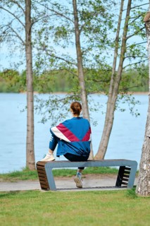 A woman sits on a unique bench facing a serene lake, surrounded by trees. She enjoys the tranquil