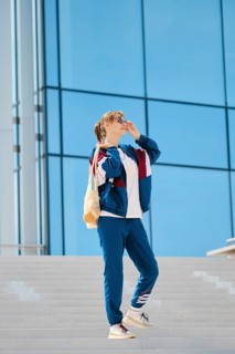 A young individual stands on a staircase, wearing sporty clothing and sunglasses. The sunny weather