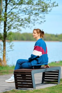 A young woman relaxes on a modern bench near a serene lake, dressed in colorful activewear. The