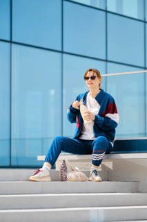 A young woman dresses in a stylish tracksuit sits on outdoor steps near a contemporary structure.