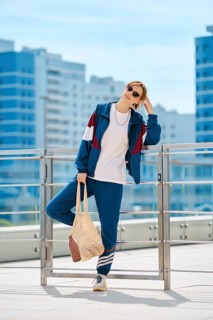 A woman dressed in a sporty outfit stands confidently on a terrace surrounded by a bright blue sky