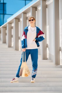 A young woman stands on a series of outdoor steps, wearing a colorful sports outfit with sunglasses