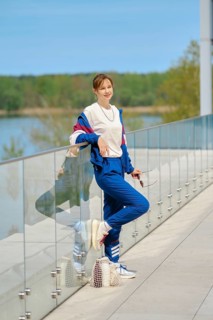 A woman dressed in comfortable sportswear leans casually against a glass railing overlooking a