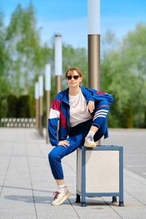 A woman dressed in a blue and maroon sporty outfit sits on a trashcan with one leg raised,