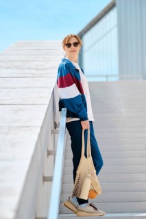 A young sporty woman with string bag stands on a staircase, dressed in stylish athletic track suit