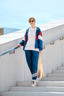 A young woman with sunglasses descends a staircase wearing a colorful sporty outfit. She carries a