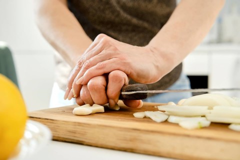 Unrecognizable woman crush garlic to finely chop it for sauce on a wooden cutting board in a bright