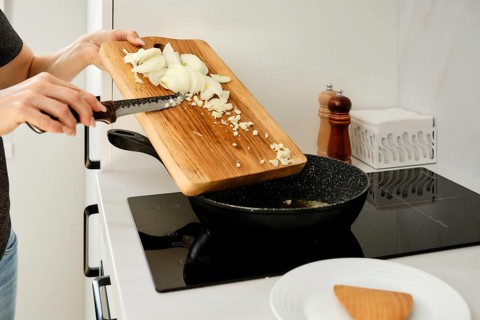 An unrecognizable woman laid out chopped onions and garlic in a frying pan. She is preparing the