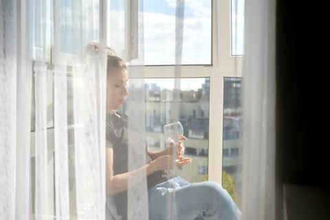 Sunlight streams through sheer curtains as a woman sits peacefully by the window. She gazes