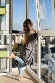 A joyful woman with long hair leans against the open window, taking in fresh air and sunlight