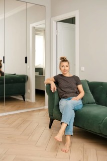A woman sits comfortably on a green couch in a modern living room. She poses casually, with her
