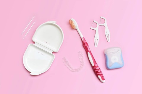 Top view of dental clear aligners, toothbrush, toothpicks and floss on pink background with copy
