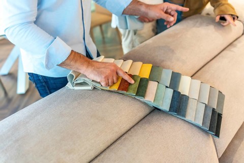 Interior designer showing fabric swatches to client, choosing upholstery for new sofa in furniture
